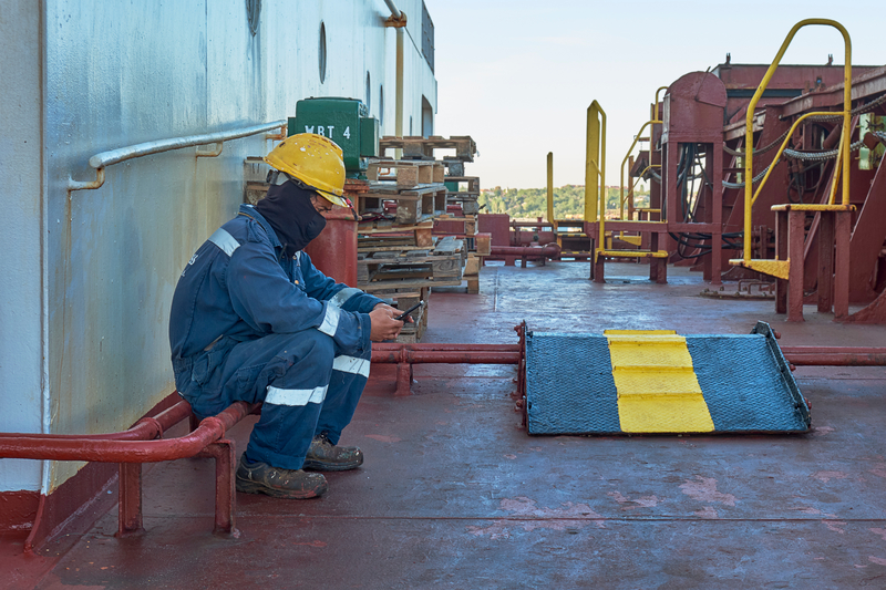 seafarer sits alone on the deck of a rusty looking ship, wearing protective clothing for his job